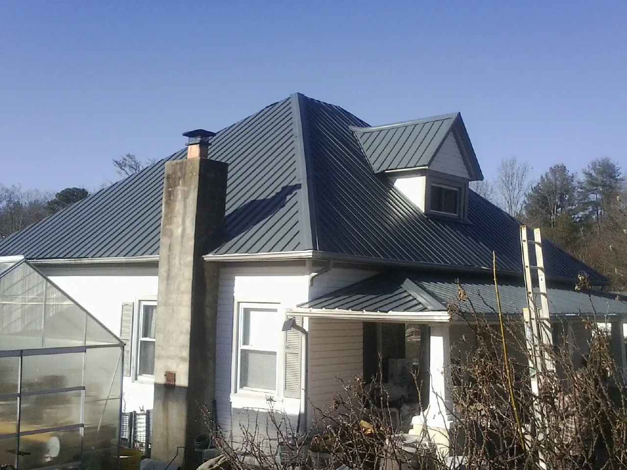 Dark blue standing seam metal roof on a white farmhouse with dormer — Slate & Tile Roof Repair by Roofing Brothers in Millican