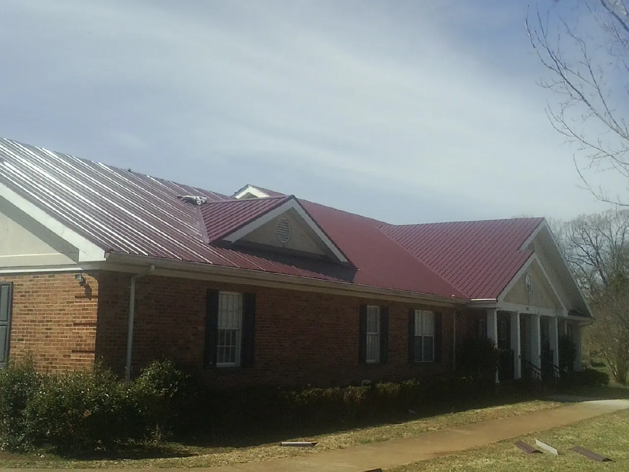 Red metal roof with gabled entries on a long brick building, from a Hail Damage Roof Repair job in Millican