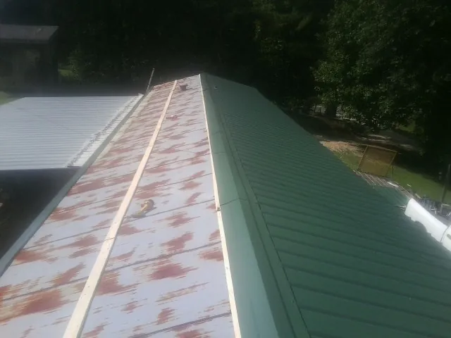 Old rusted panels beside newly installed green metal roofing — Wind Damage Roof Repair by Roofing Brothers in Millican