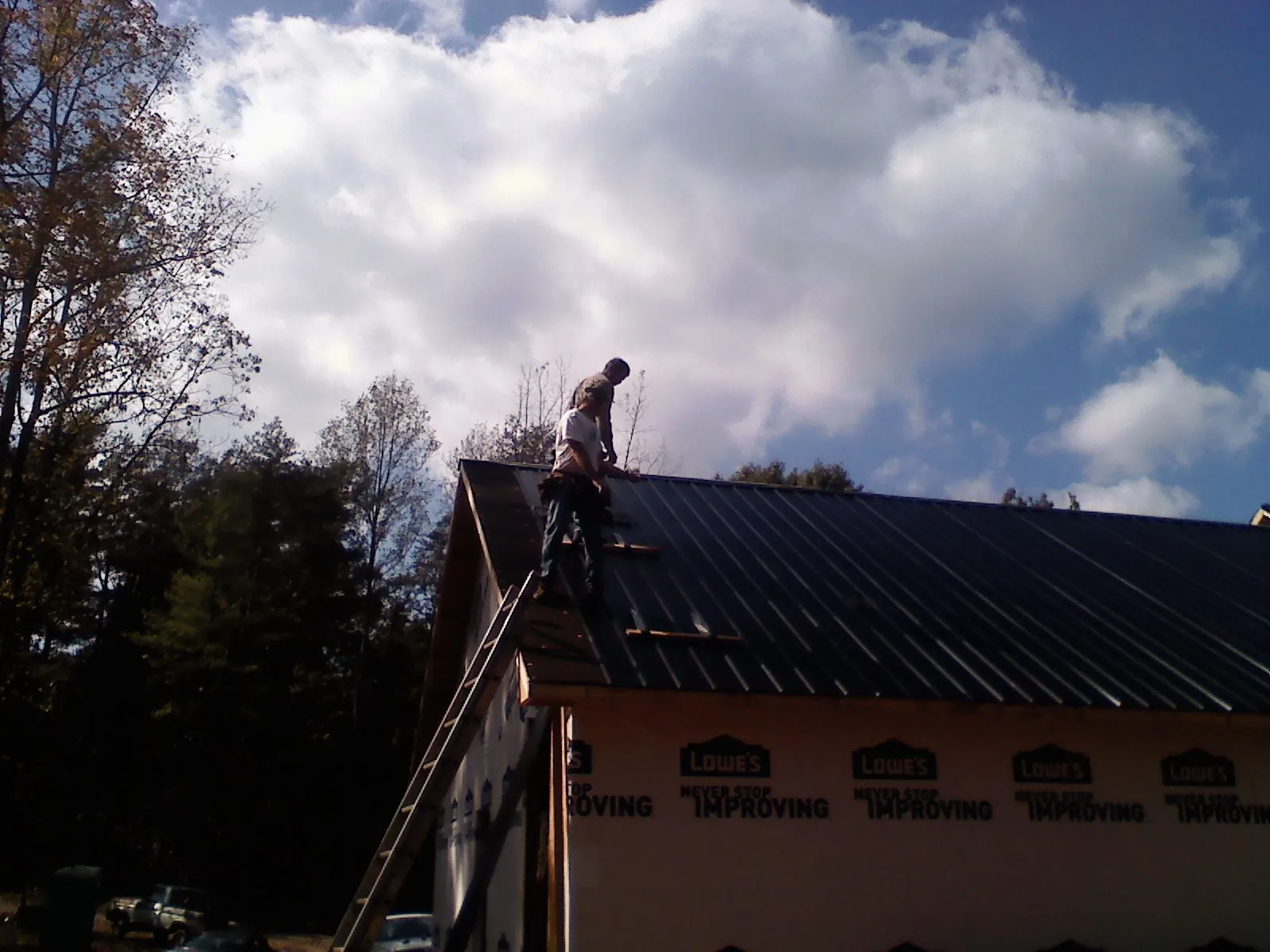 Roofer fastening dark metal panels high against a cloudy sky, from a Roof Inspection job in Millican