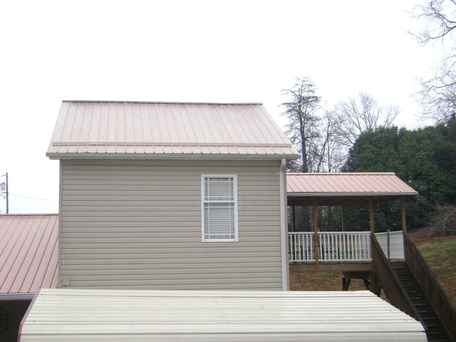 Tan metal roofs on a two story addition and attached porch, from a Roof Replacement job in Millican